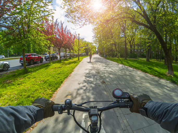 Montar un scooter eléctrico en un carril bici cuando hace sol. Vista en primera persona.